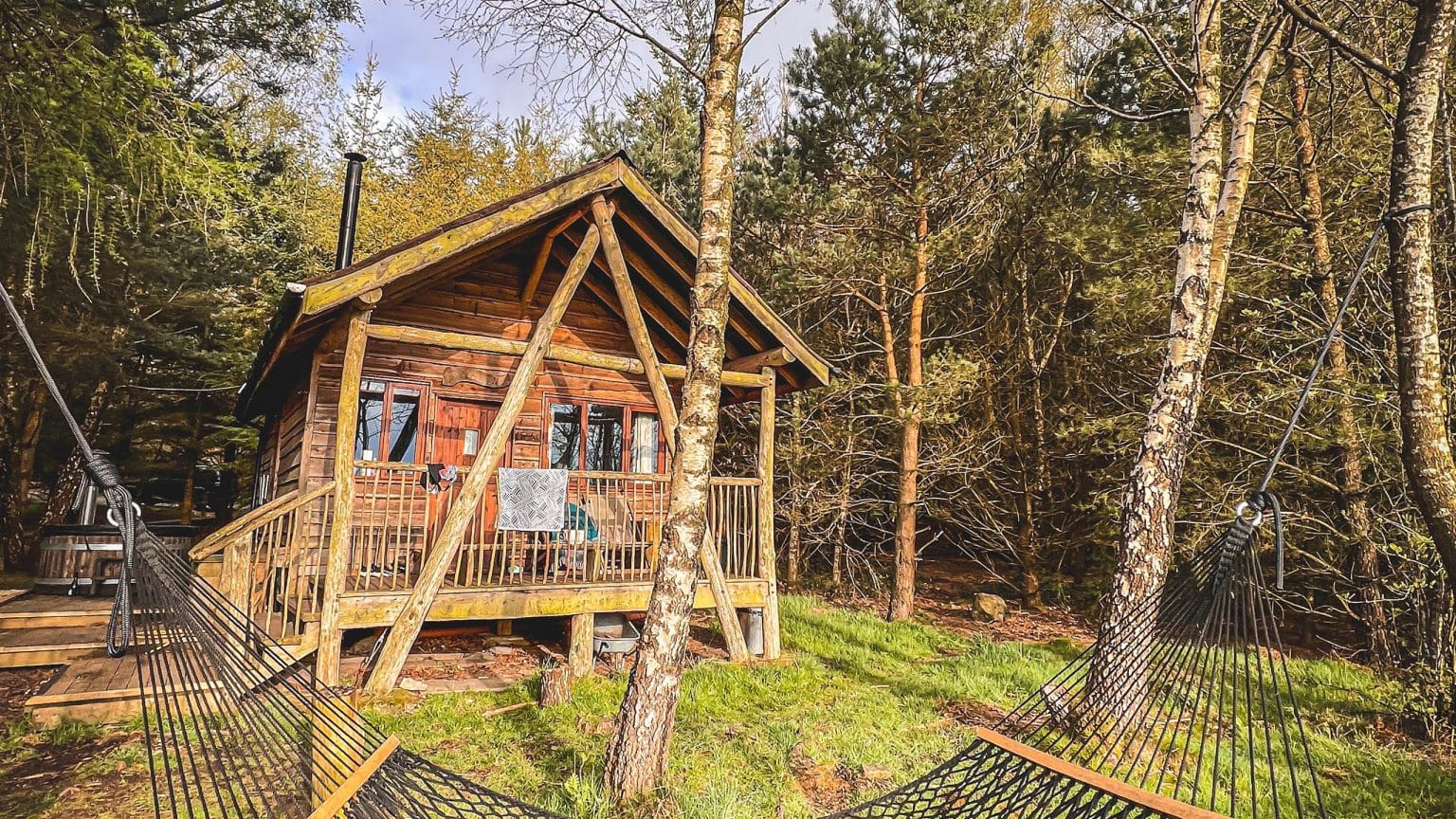 Off-grid cabin at Swinton Bivouac, nestled in a woodland setting with a wooden deck