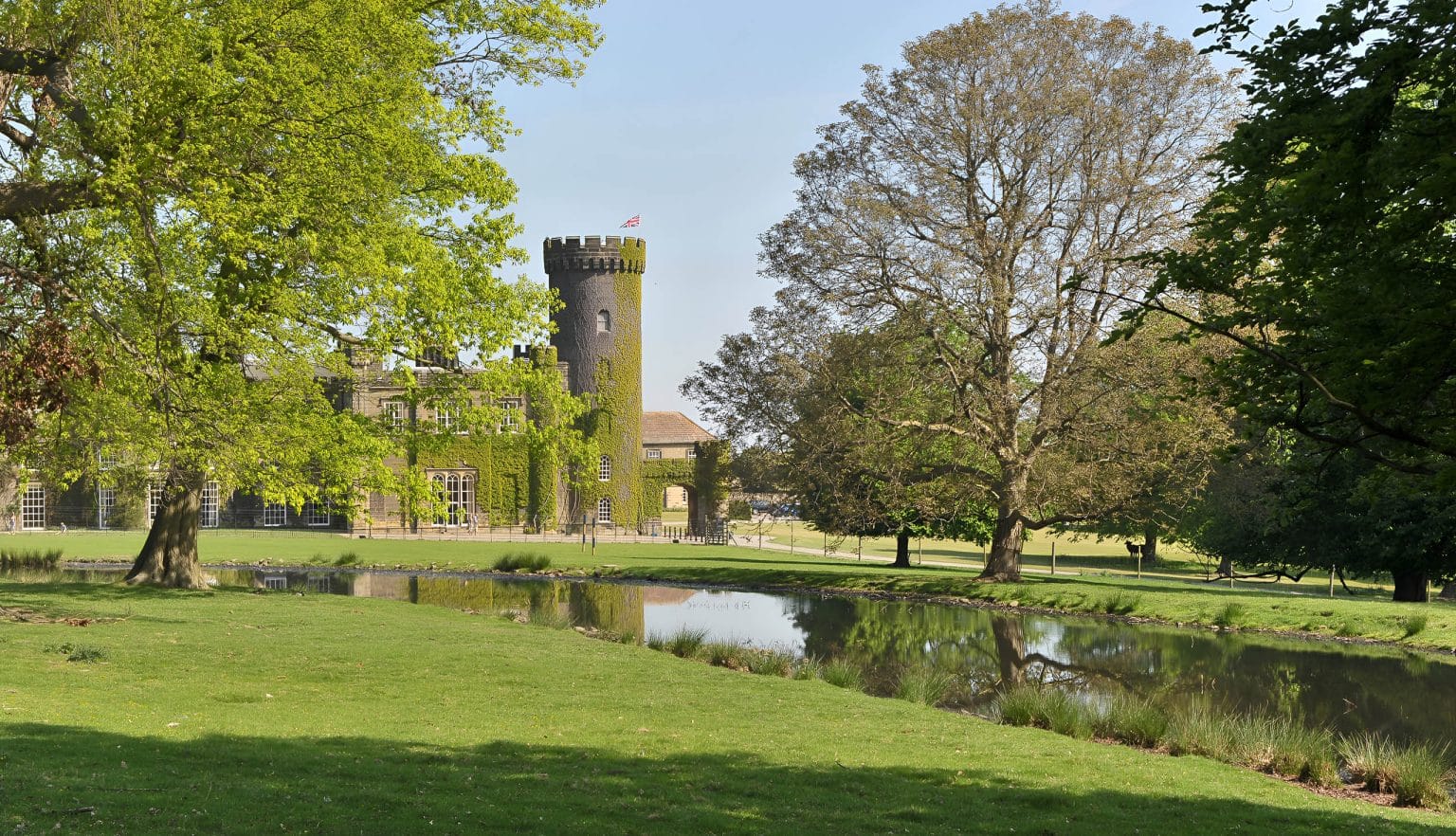Swinton Park Hotel surrounded by lush parkland and a reflective water feature