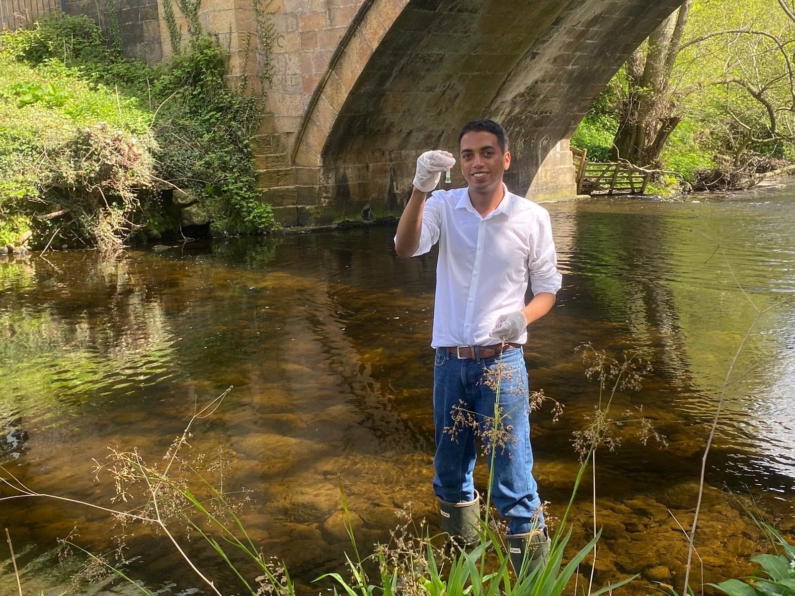 David Hay standing in a river holding a water sample